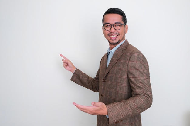 Photo homme d'affaires asiatique portant un costume marron souriant heureux tout en pointant le doigt sur un espace blanc derrière