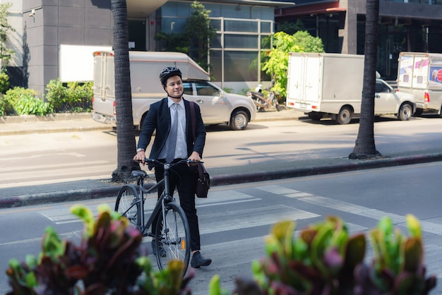 Homme d'affaires asiatique pousse un vélo sur un passage pour piétons sur une rue de la ville au cours d'un trajet du matin