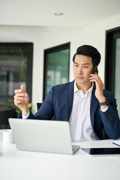 Homme d'affaires asiatique professionnel parlant au téléphone tout en travaillant dans son bureau