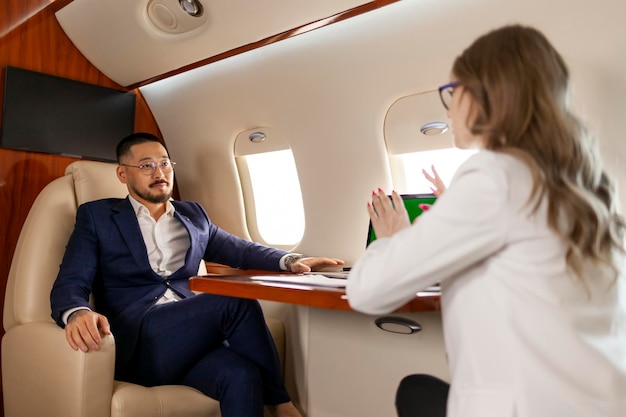 Un homme d'affaires asiatique prospère en costume à la réunion avec une femme d'affaires partenaire dans un jet privé