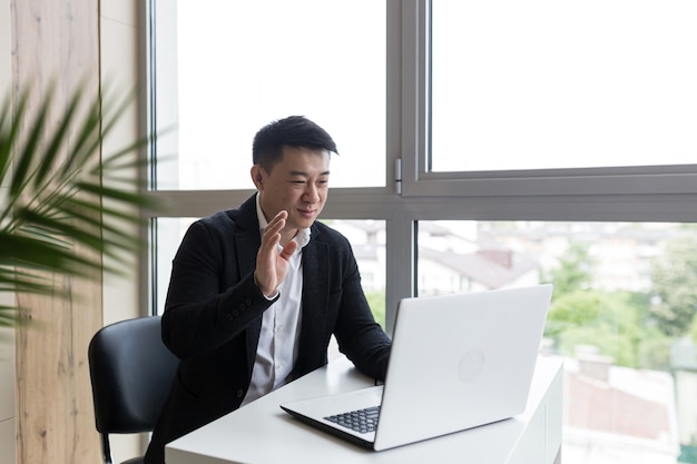 homme d'affaires asiatique prospère dans un costume noir travaille sur un ordinateur portable dans un bureau élégant