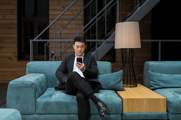 Homme d'affaires asiatique prospère dans un costume noir utilise le téléphone