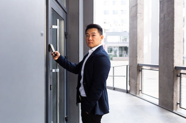 Un homme d'affaires asiatique prospère ouvre la porte du centre de bureaux à l'aide d'un smartphone et d'une application NFC