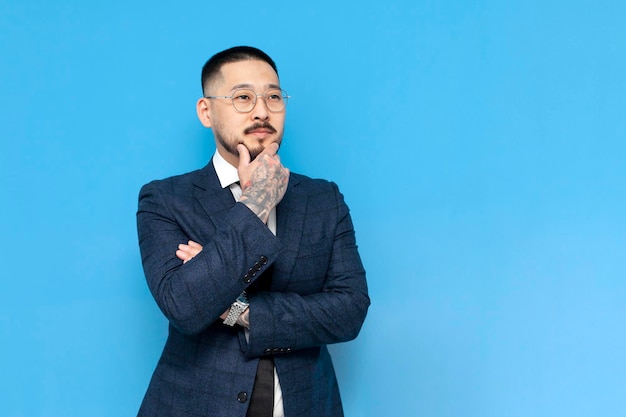 Un homme d'affaires asiatique réfléchi et prospère en costume et lunettes pense et regarde l'espace de copie.