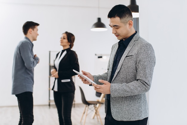 Homme d'affaires asiatique avec sa tablette, groupe de personnes au bureau lumineux moderne à l'intérieur