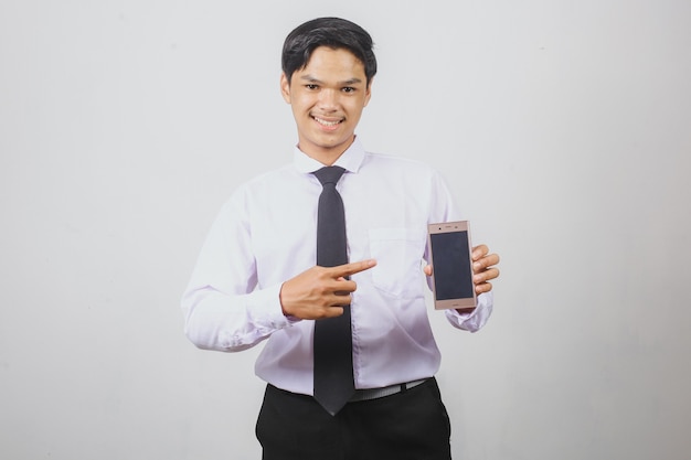 Homme d'affaires asiatique souriant en chemise blanche et cravate noire pointant vers l'écran vide du téléphone intelligent