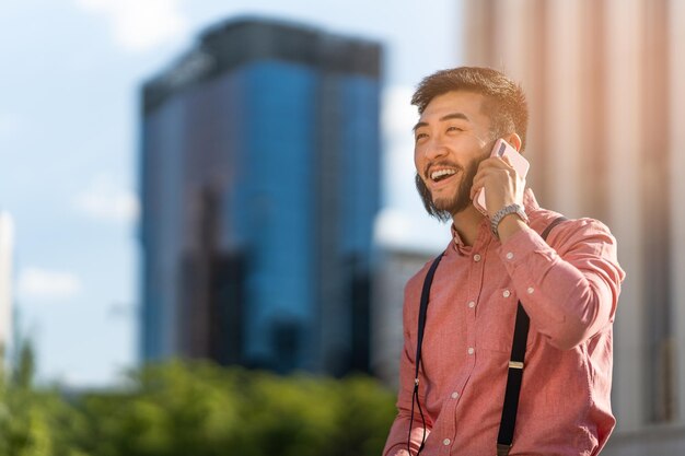 Homme d'affaires asiatique souriant parlant au mobile à l'extérieur