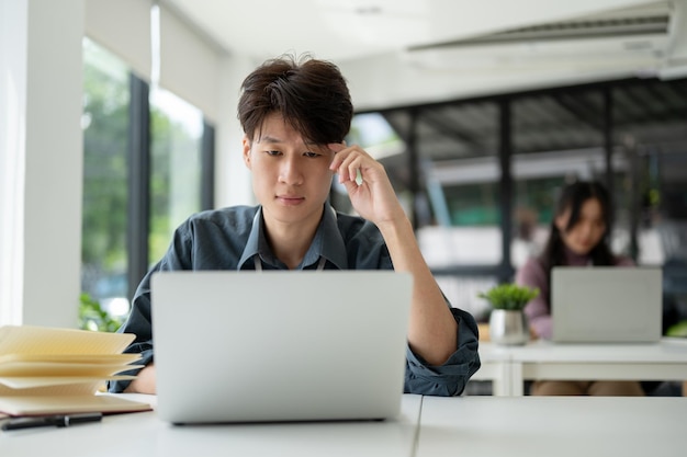 Un homme d'affaires asiatique stressé regarde pensivement son ordinateur portable en pensant à son projet