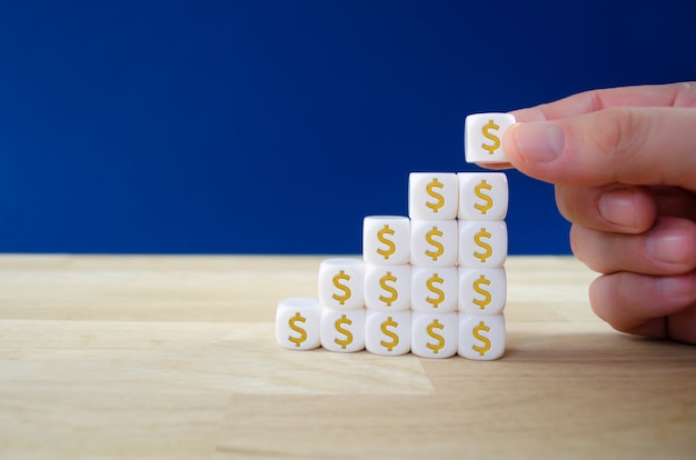 Homme d'affaires, assemblage de dés blancs avec des signes de dollar en or en forme de graphique de croissance dans une image conceptuelle de la croissance financière.