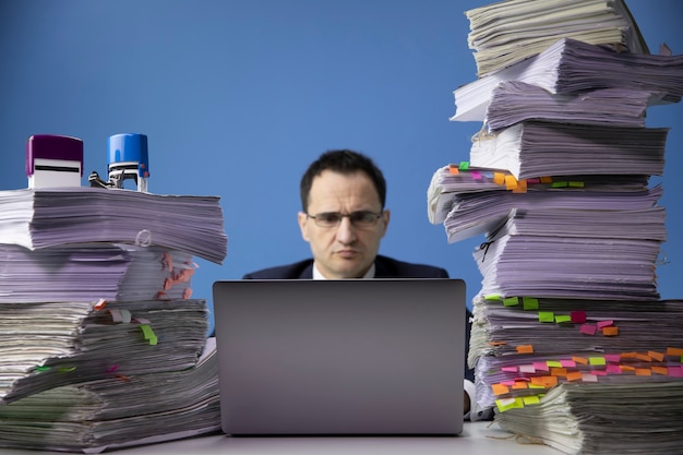 Homme d'affaires assis au bureau avec une énorme pile de documents