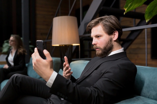 homme d'affaires assis dans un restaurant élégant dans un costume d'affaires relaxant et utilise le téléphone pour communiquer