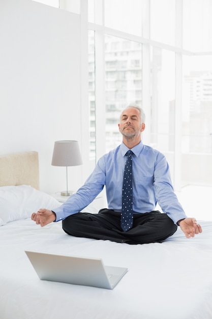 Homme d&#39;affaires assis en posture de lotus avec ordinateur portable sur le lit