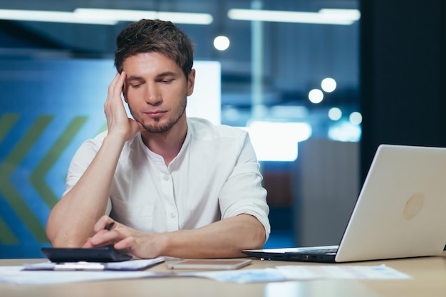 Homme d'affaires au bureau pensant au bureau travaillant avec des documents et calculant des rapports sur une calculatrice