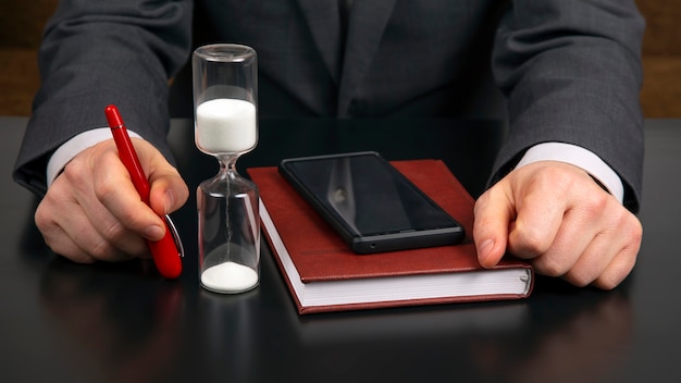 L'homme d'affaires au bureau travaille avec un téléphone mobile sur le d'un sablier