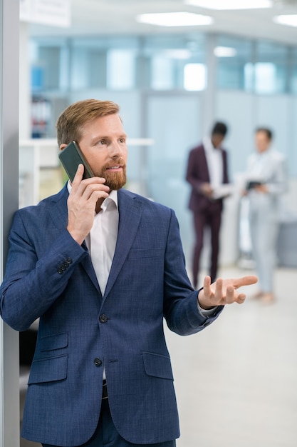 Homme d'affaires barbu communiquant sur smartphone contre deux collègues