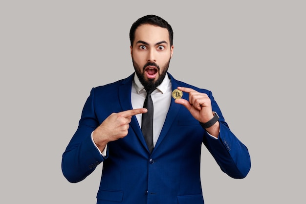 Homme d'affaires barbu surpris tenant un doigt pointé sur la monnaie crypto de commerce électronique bitcoin d'or