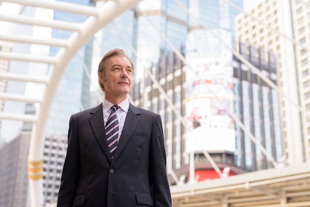 Homme d'affaires beau mature en costume pensant au pont de skywalk dans la ville