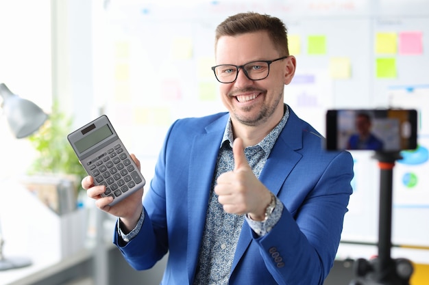 Un homme d'affaires blogueur souriant tient une calculatrice et enregistre des vidéos de formation sur les revenus