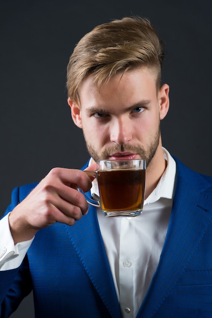 L'homme d'affaires boit une tasse de thé en veste bleue, chemise blanche sur fond gris. Concept de pause-café de bureau. Affaires et entrepreneuriat.