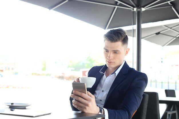 Homme d'affaires buvant une tasse de café assis avec son téléphone au café.