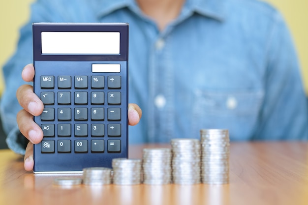 Un homme d'affaires avec une calculatrice et une pile de pièces en premier plan