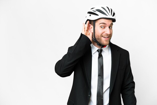 Homme d'affaires avec un casque de vélo sur fond blanc isolé écoutant quelque chose en mettant la main sur l'oreille