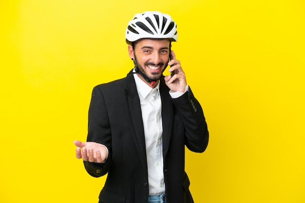 Homme d'affaires caucasien avec un casque de vélo isolé sur fond jaune en gardant une conversation avec le téléphone portable avec quelqu'un