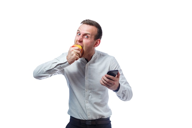 Homme d'affaires caucasien tenant un téléphone portable en noir et tenant une pomme rouge-jaune. Il porte une chemise. Portrait émotionnel. Isolé sur fond blanc