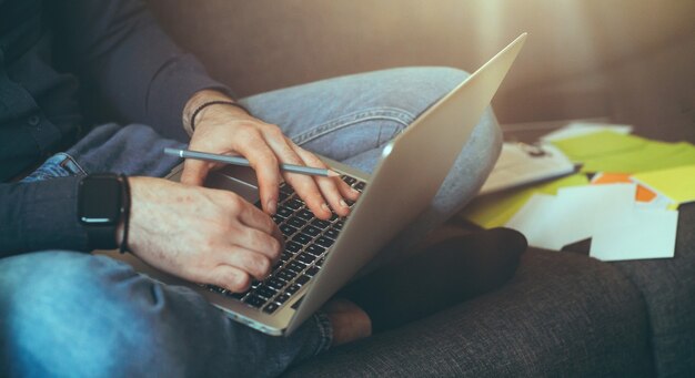 Homme d'affaires caucasien travaillant à la maison avec un ordinateur portable et des documents assis sur le canapé