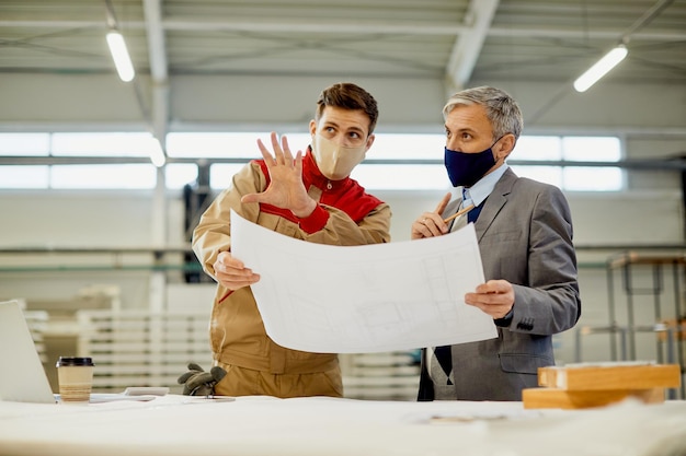 Homme d'affaires et charpentier d'âge moyen analysant des plans dans une installation industrielle