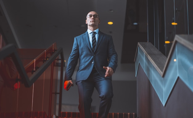 Photo sûr homme d'affaires chauve mature marchant dans les escaliers avec smartphone à la main. beau