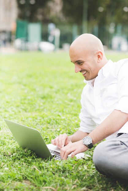 Homme d&#39;affaires en chemise blanche travaillant avec ordinateur portable sur l&#39;herbe dans un parc