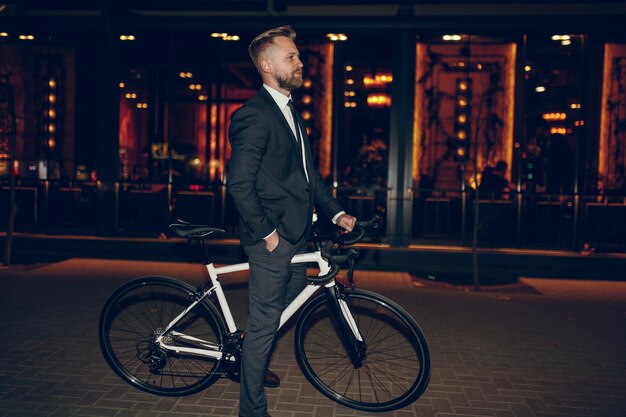 Homme d'affaires chic avec vélo debout sur la rue de la ville de nuit