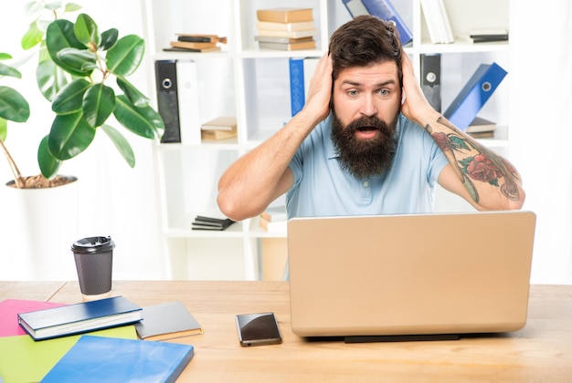 Un homme d'affaires choqué s'accrochant à la tête en regardant son ordinateur portable sur son bureau.