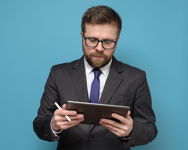Homme d'affaires concentré en costume fonctionne avec une tablette et un stylet isolé sur fond bleu