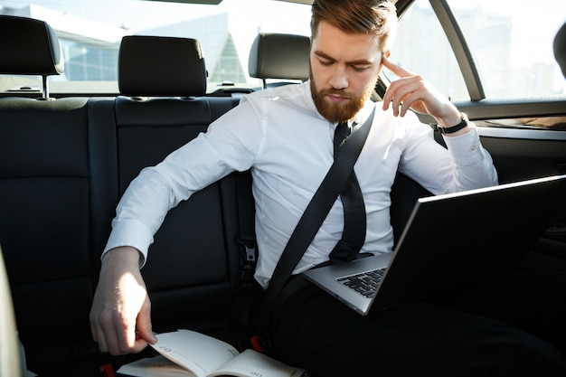 Homme d'affaires concentré avec ordinateur portable en regardant portable