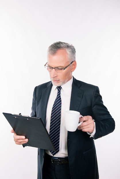 Homme d'affaires confiant âgé avec des lunettes, lire des informations dans un dossier contenant une tasse