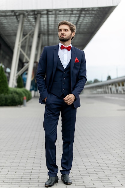 Homme d'affaires confiant. Confiant jeune homme en costume complet ajustant sa manche et en détournant les yeux tout en se tenant à l'extérieur avec le paysage urbain en arrière-plan