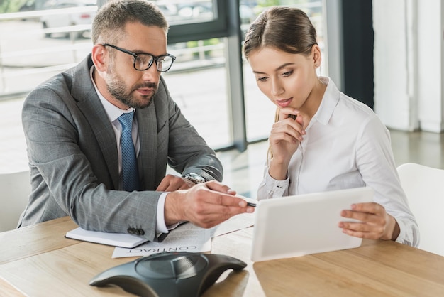 Homme d'affaires confiant et femme d'affaires regardant une tablette ensemble dans un bureau moderne