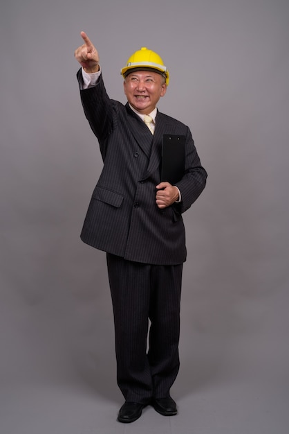 Homme d'affaires de construction asiatique mature contre mur gris