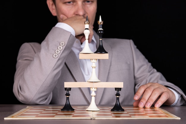 Un homme d'affaires construit une pyramide de pièces d'échecs et de blocs de bois