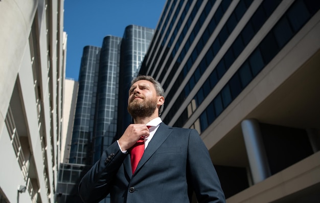 Homme d'affaires en costume bleu attachant la cravate en plein air homme d'affaires bien habillé sur l'immeuble de bureaux de la ville