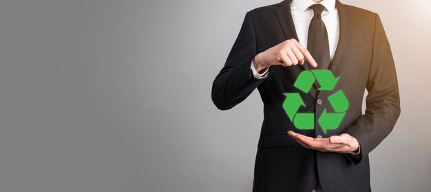 Homme d'affaires en costume sur fond gris détient une icône de recyclage, signe dans ses mains. Concept d'écologie, d'environnement et de conservation