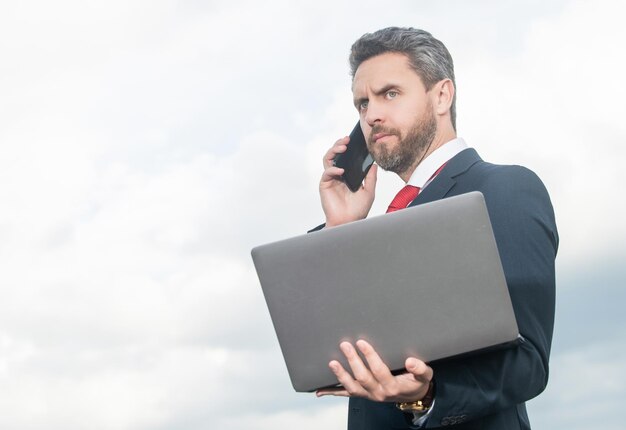 Homme d'affaires en costume parlant au téléphone et tenant l'ordinateur