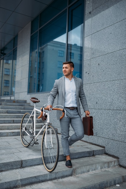 Homme d'affaires en costume avec vélo descend les escaliers de l'immeuble de bureaux au centre-ville.