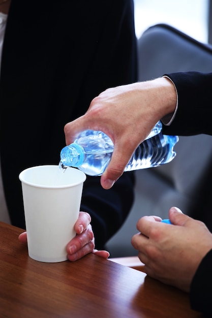 Homme d'affaires en costume versant de l'eau d'une bouteille dans une tasse en papier lors d'une réunion d'affaires