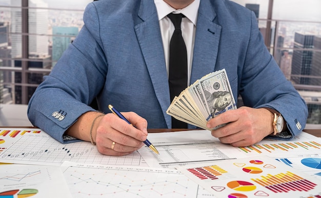 Un homme d'affaires avec une cravate examine les graphiques de profit et calcule les dépenses en dollars