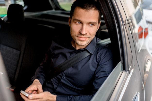 Homme d'affaires dans un taxi est titulaire d'un smartphone et regarde par la fenêtre. Promenades des passagers dans le portrait en gros plan du siège arrière