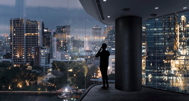 Homme d'affaires debout à l'aide d'un téléphone intelligent dans un espace moderne regardant la vue nocturne de la ville