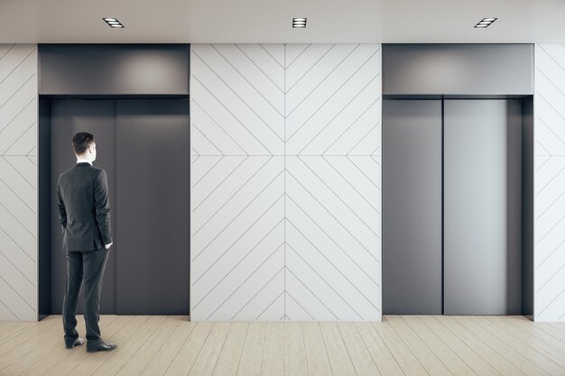 Homme d'affaires debout dans un hall de bureau contemporain avec deux ascenseurs